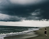 Big Big World- photographic print of a girl on the beach, with stormy dark blue sky above the ocean, Outer Banks