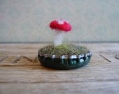 Felted amanita mushroom in a dark green metallic bottlecap