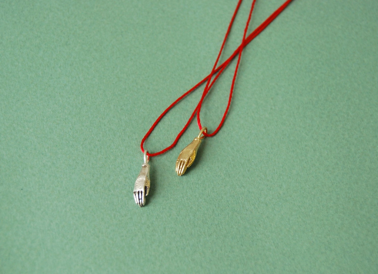 Silver hand on red silk cord