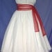 A stunning one-strap 50s style cocktail dress with a beautiful waist defining red sash.