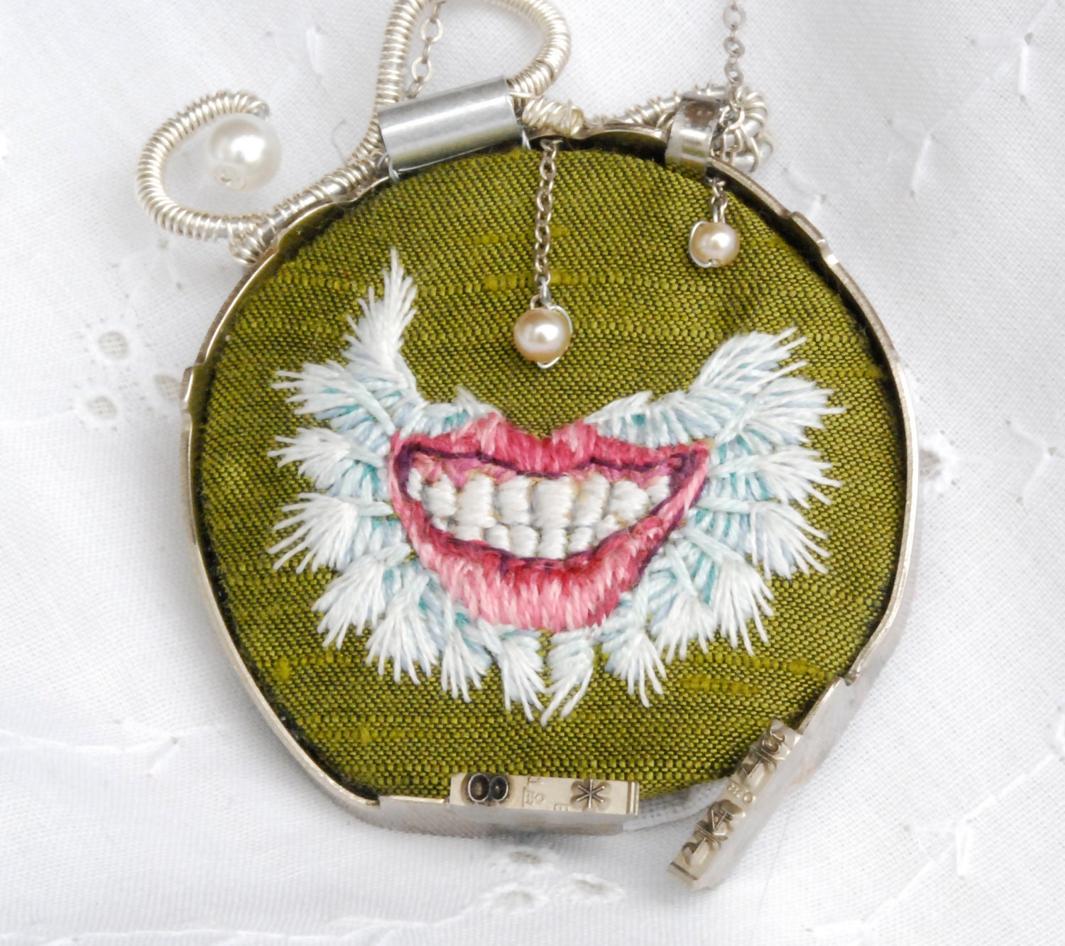 Green embroidered necklace of a mightily winged smile wrapped in typewriter keys "Pneumothorax"