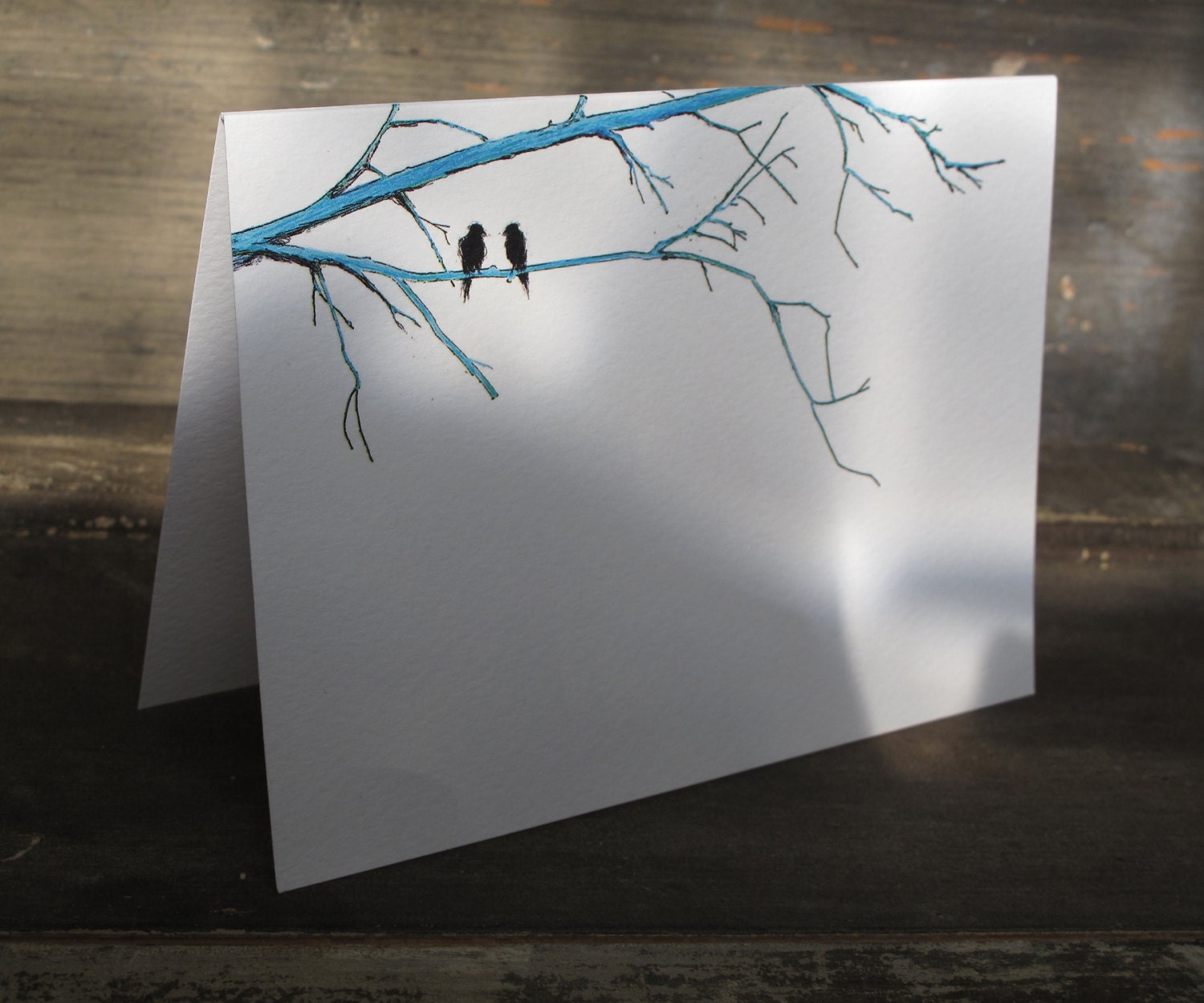 A  greeting card on artist watercolor paper with one of my original illustrations of two black birds perched on blue branches