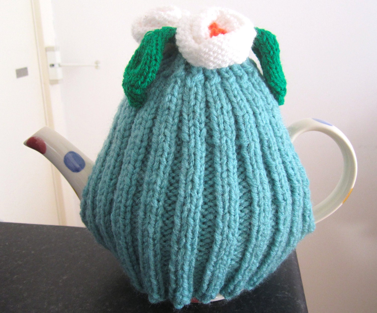 Teal green knitted teapot cozy with lily design.