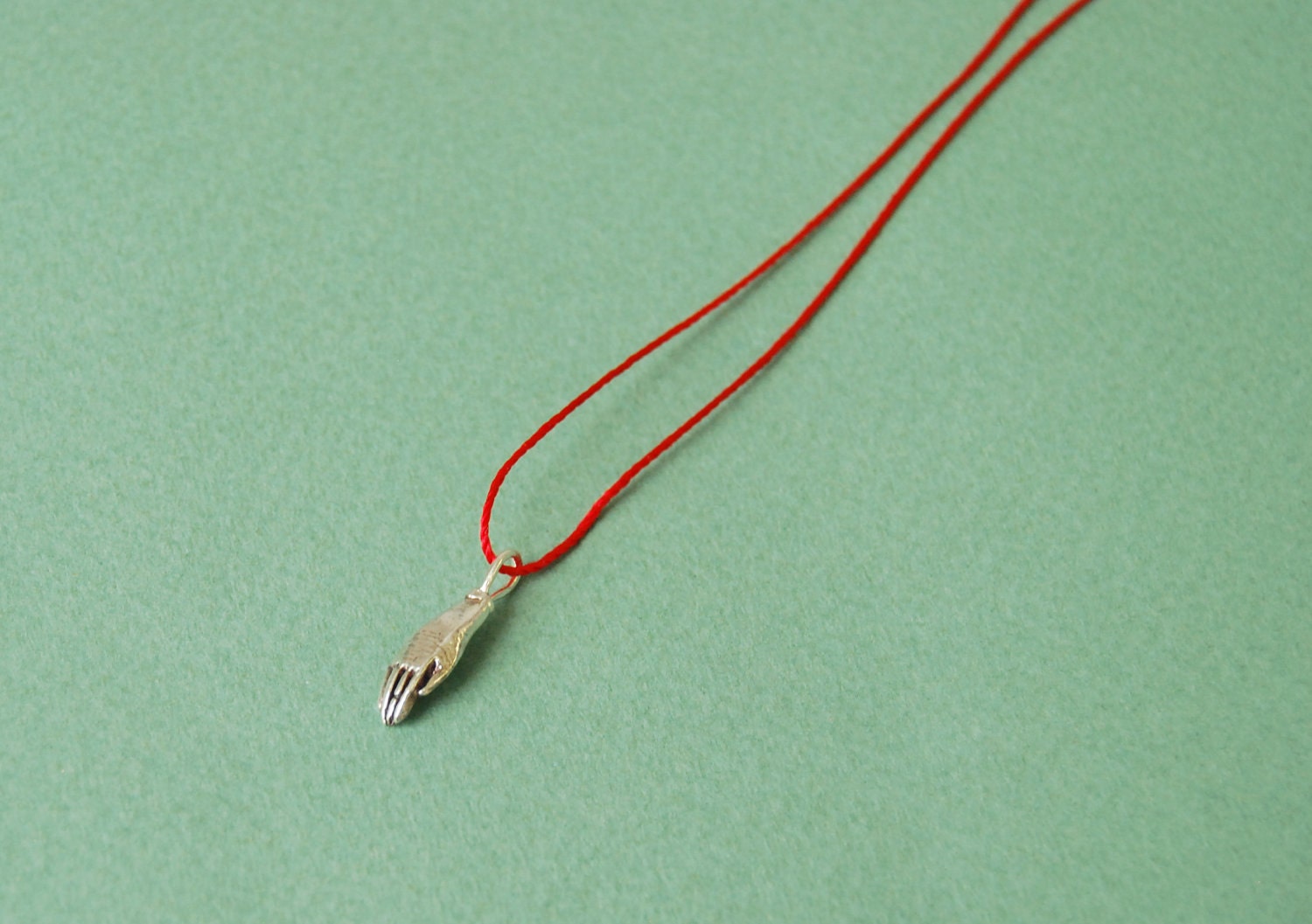 Silver hand on red silk cord