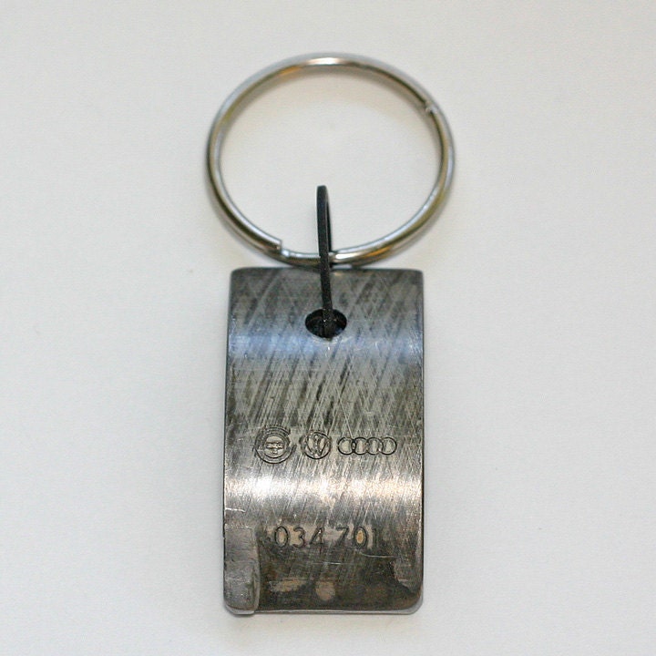Car Part KEYCHAIN - AUDI part with original stampings of logo and part numbers.  Black velvet backing.