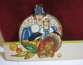 1920's-30's die cut place card thanksgiving theme with male and female pilgrims and turkey, and fall harvest gold gilded hallmark