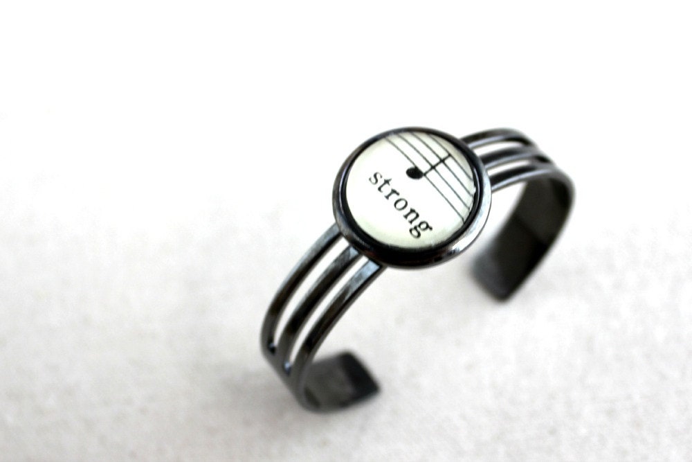 Unisex cuff bracelet for man or woman in shiny gunmetal black adjustable made with vintage sheet music uplifting word strong