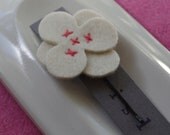 White wool felt flower hair clip with red stitching.