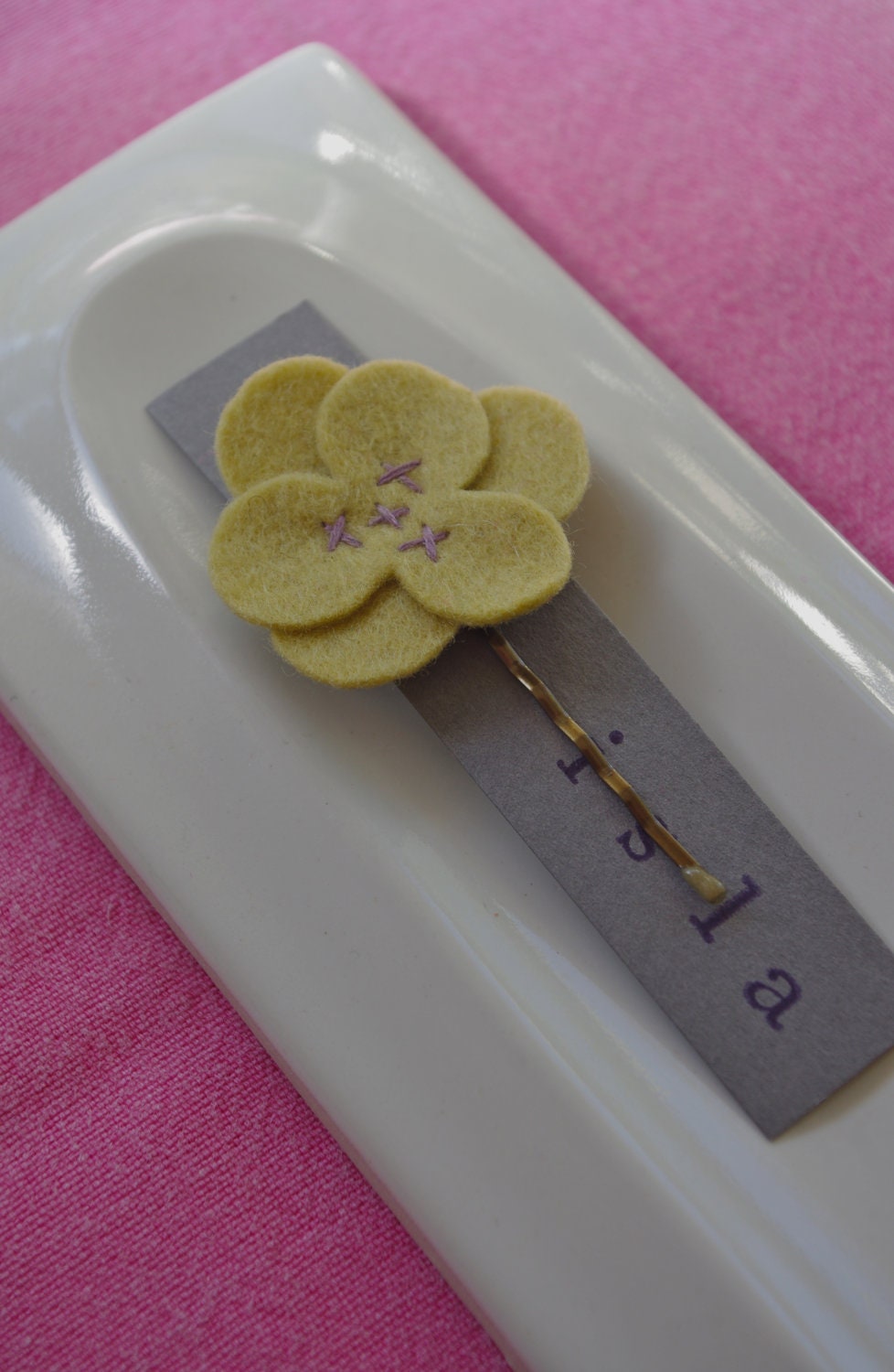Yellow wool felt flower hair clip with purple stitching.