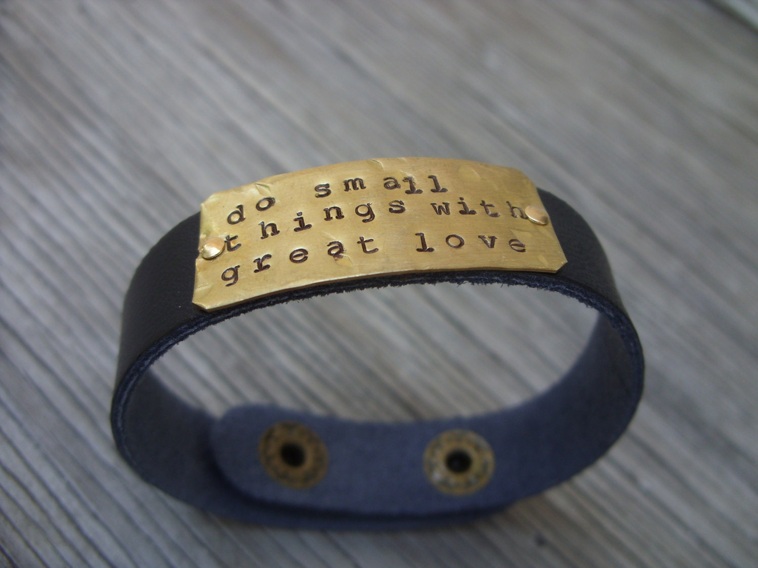 A riveted, brown leather cuff bracelet with hand stamped brass do small things with great love- distressed and embellished wording