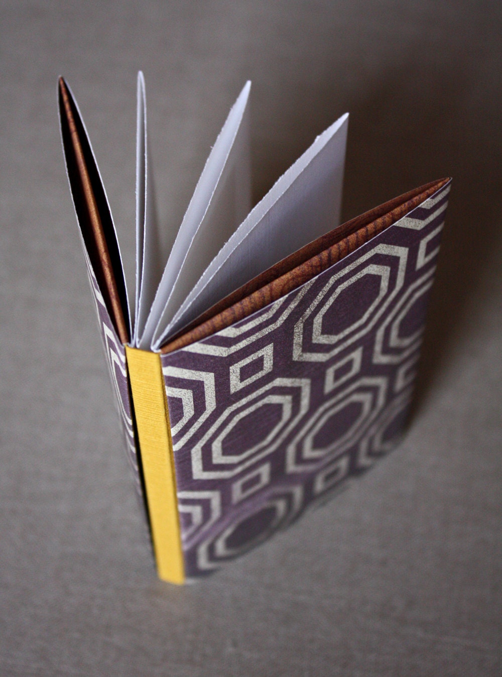 Concertina book with geometric eggplant-colored cover and mustard spine