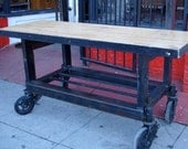 Rolling work table with butcher block slab top on a black steel frame with lower shelf and large 8 inch wheels