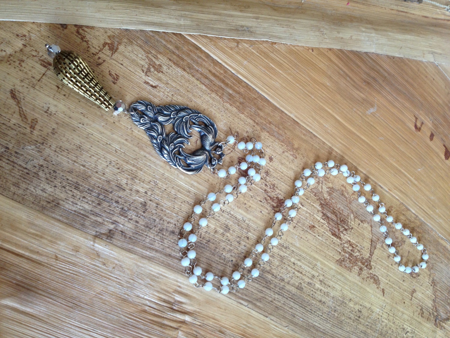 White rosary necklace with peacock finding and gold charm.