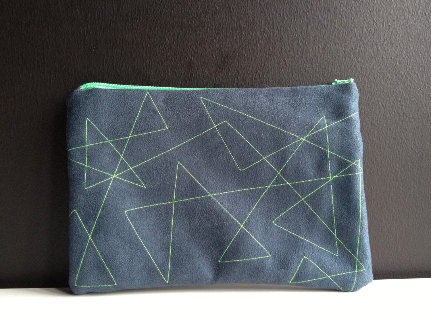 dark blue pouch made of faux leather with stitched geometric lines in neon green