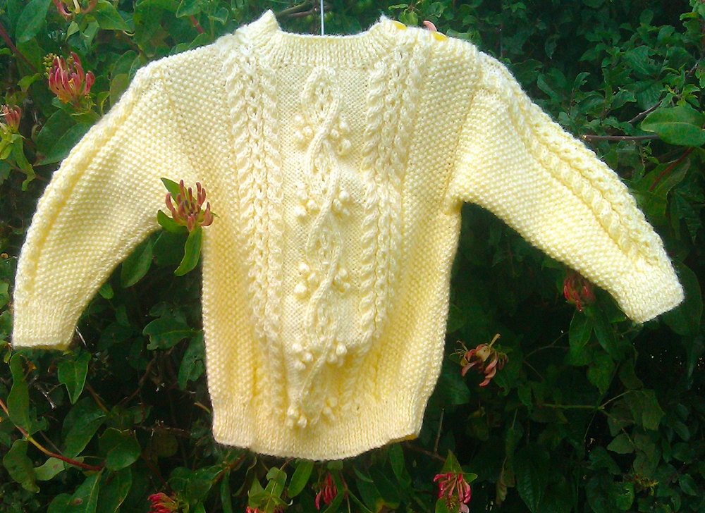 Child's handknit yellow aran sweater with shoulder opening.