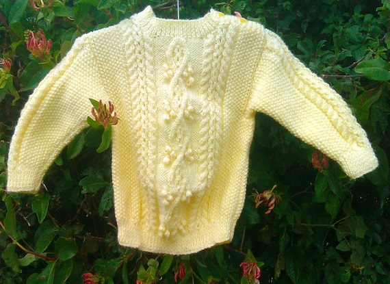 Child's handknit yellow aran sweater with shoulder opening.