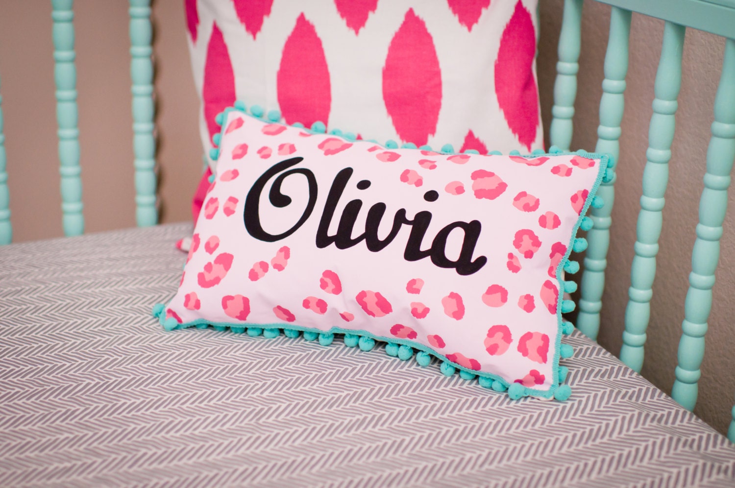 Baby pillow in bright pink leopard print and turquoise pom pom trim. Personalized with name.