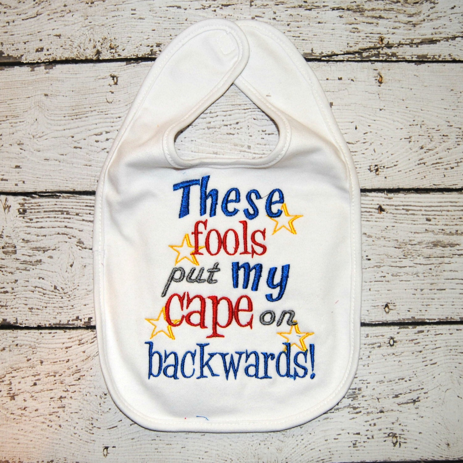 Embroidered Bib With The Saying "These Fools Put My Cape On Backwards