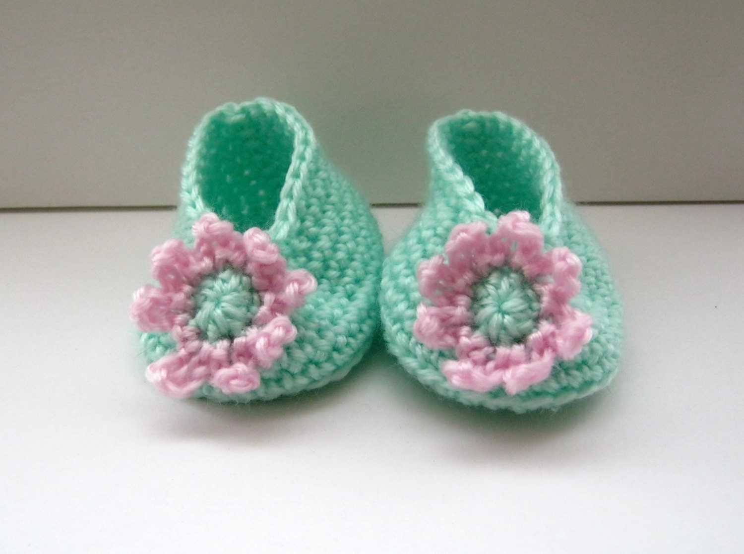 Crocheted baby booties in mint green with a pale pink and mint green flower