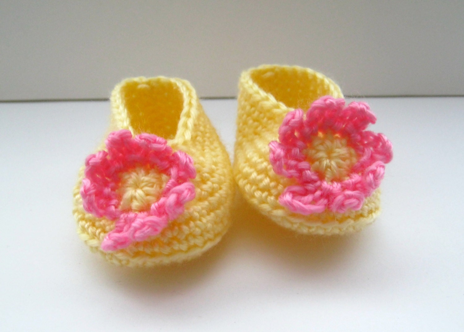 Crocheted baby booties in primrose yellow with a pink and yellow flower