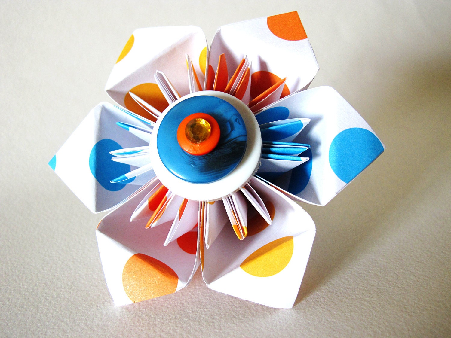 6 petal geometric star in blue orange yellow and white with center buttons.