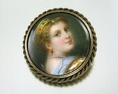 Victorian hand painted portrait on porcelain brooch. Portrait of a beautiful woman wearing her jewels. Braided brass gallery around the porcelain portrait and a straight pin stem with a C clasp on the back. A few minor wear spots as seen in the photos. Measures 1-1/4 inches across.